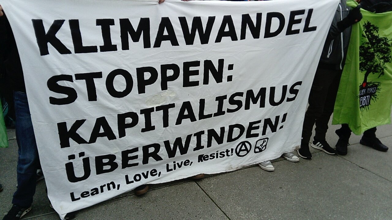 Ein Transparent mit der Aufschrift: "Klimawandel stoppen: Kapitalismus überwinden. Learn, Love, Live, Resist!